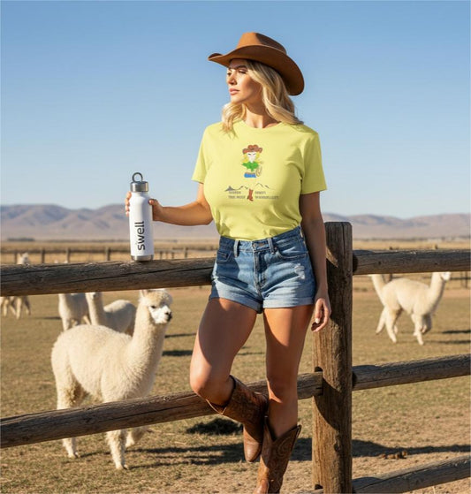 Woman in a yellow t-shirt with a cowgirl graphic and cowboy hat holding a Swell water bottle with alpacas in the background.