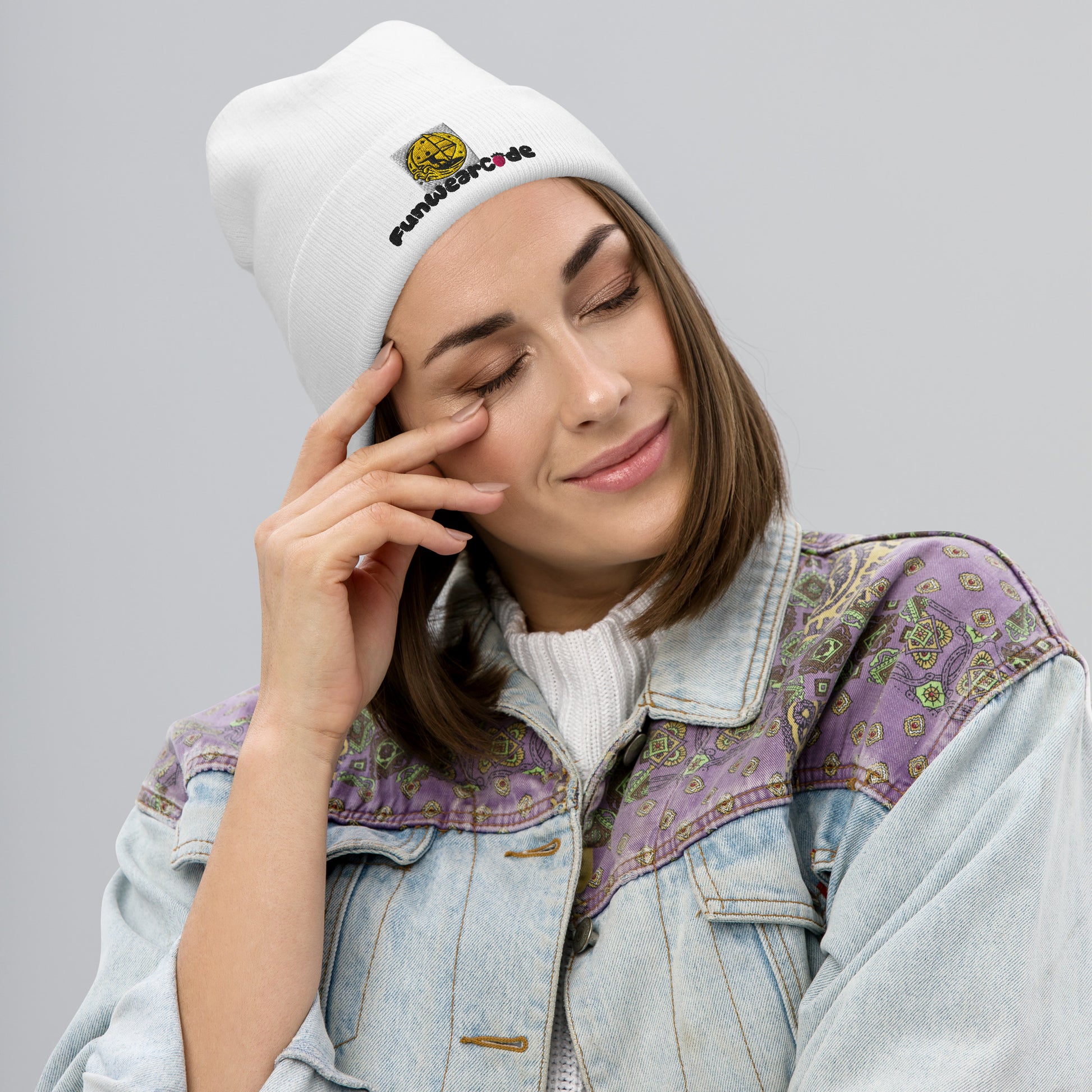 Woman wearing a white "FunWearCode" branding beanie with embroidery and a patterned denim jacket on a gray background