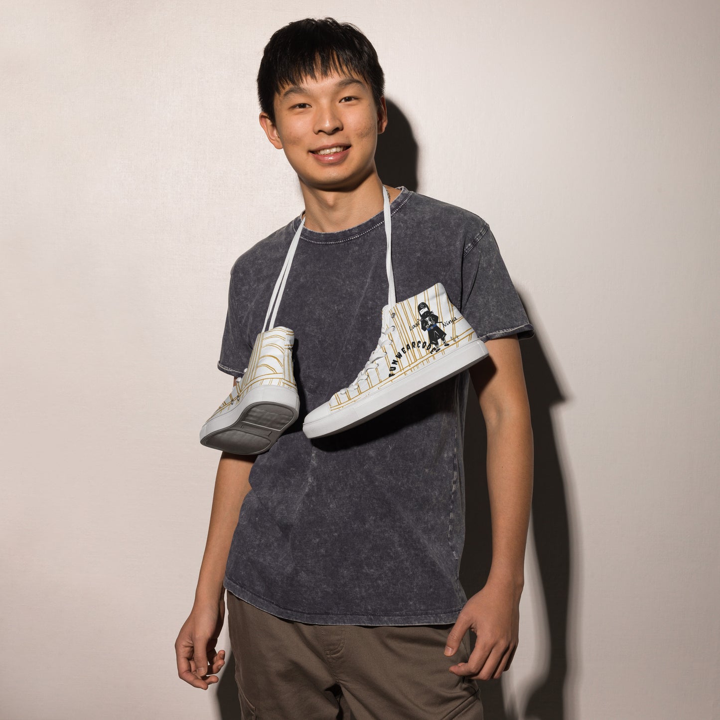 Person holding two white high-top sneakers with a ninja graphic and 'Fun Wear Code' text logo against a plain background